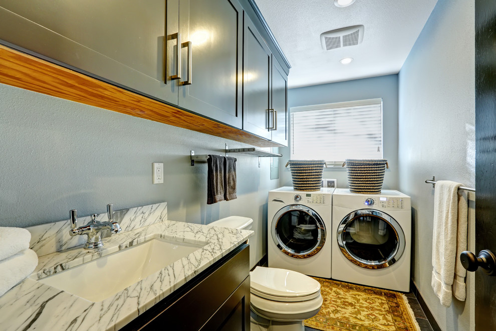 This is an example of a small contemporary l-shaped utility room in Other with an undermount sink, shaker cabinets, green cabinets, a side-by-side washer and dryer, brown floor, white benchtop and grey walls.
