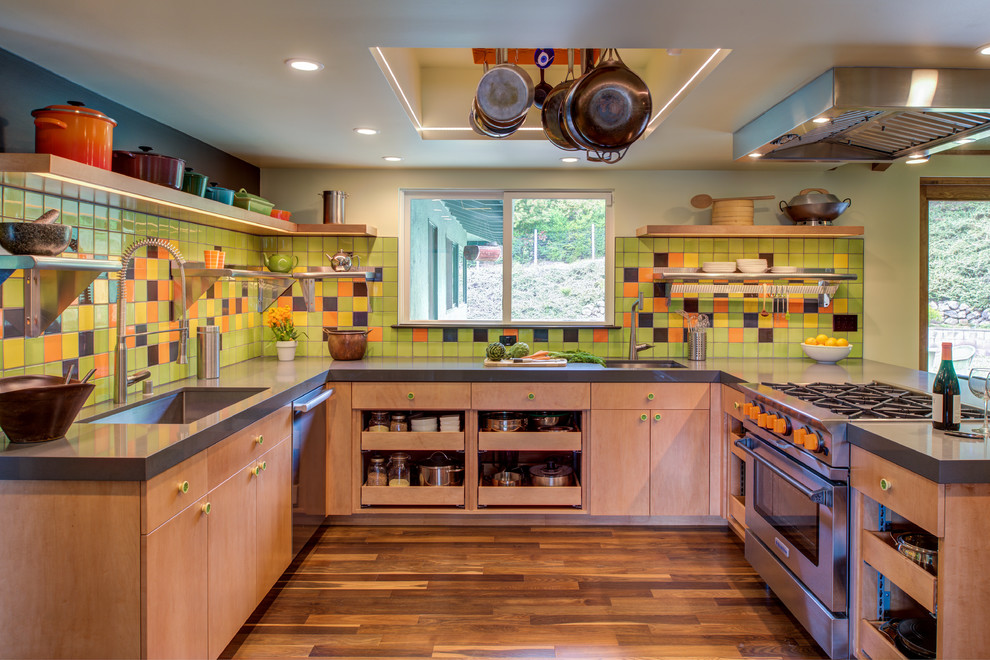 This is an example of a mid-sized midcentury u-shaped kitchen in San Francisco with an undermount sink, flat-panel cabinets, multi-coloured splashback, stainless steel appliances, medium hardwood floors, a peninsula, grey benchtop and medium wood cabinets.