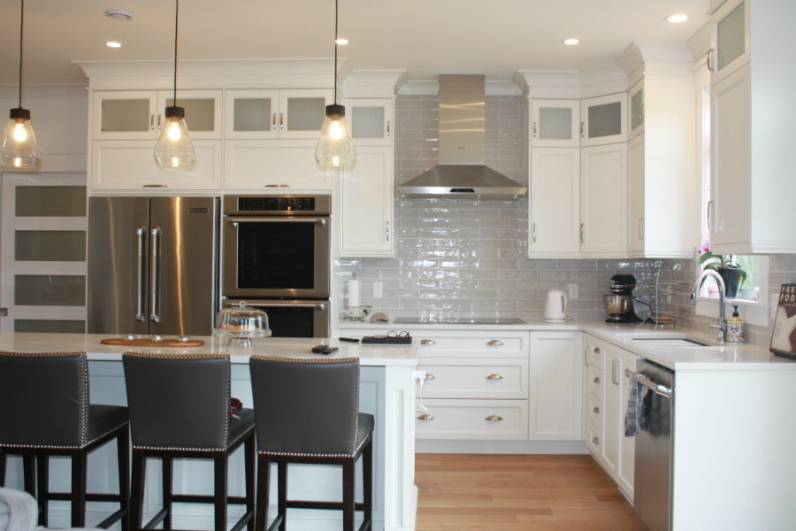 Example of a mid-sized transitional l-shaped medium tone wood floor kitchen pantry design with an undermount sink, shaker cabinets, white cabinets, quartz countertops, gray backsplash, cement tile backsplash, stainless steel appliances, an island and white countertops