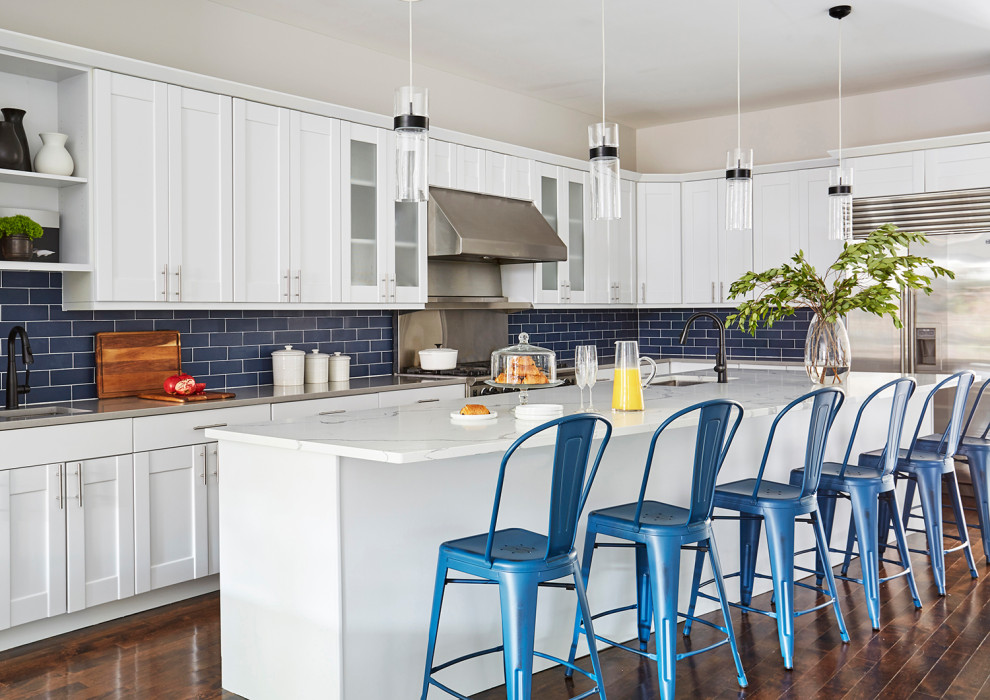 Inspiration for an expansive transitional l-shaped kitchen in Chicago with an undermount sink, shaker cabinets, white cabinets, blue splashback, stainless steel appliances, with island, brown floor, white benchtop, stainless steel benchtops, subway tile splashback and medium hardwood floors.