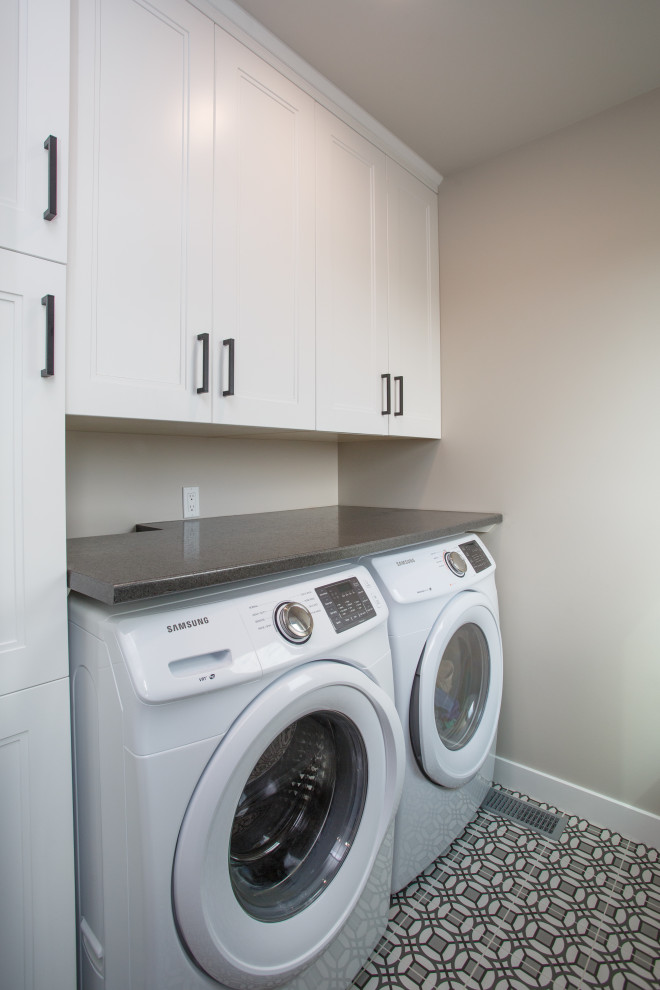 Photo of a mid-sized transitional single-wall dedicated laundry room in Calgary with recessed-panel cabinets, white cabinets, laminate benchtops, beige walls, ceramic floors, a side-by-side washer and dryer, multi-coloured floor and black benchtop.