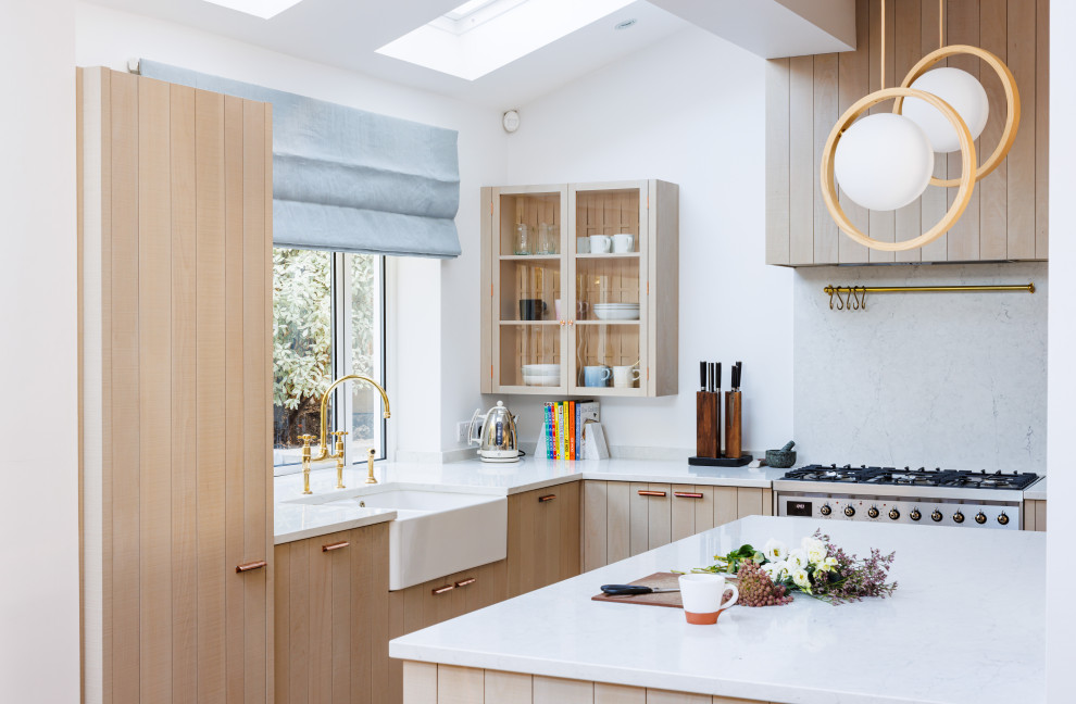 Photo of a contemporary l-shaped kitchen in London with a belfast sink, flat-panel cabinets, light wood cabinets, integrated appliances, an island, white worktops and a vaulted ceiling.