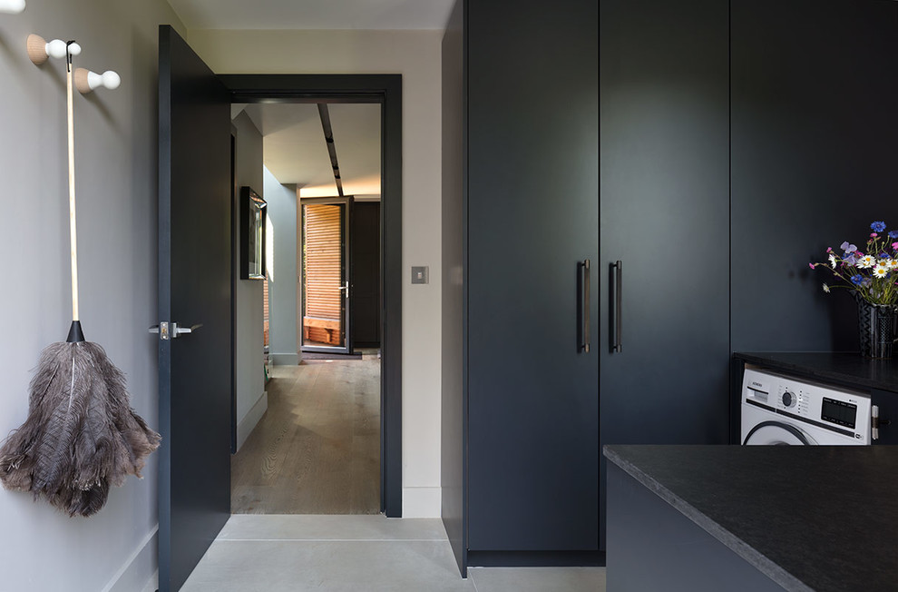 Large contemporary single-wall utility room in London with an undermount sink, marble benchtops, light hardwood floors, flat-panel cabinets, grey cabinets, grey walls, an integrated washer and dryer and black benchtop.