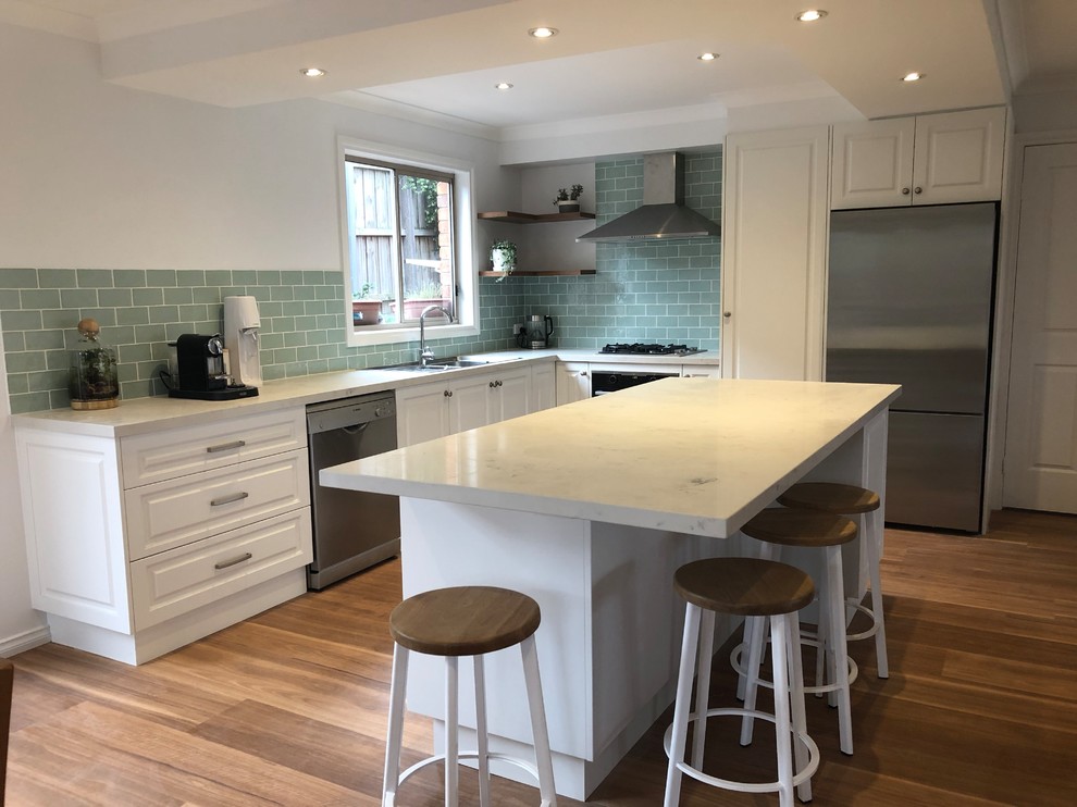 Design ideas for a mid-sized traditional l-shaped open plan kitchen in Melbourne with a drop-in sink, raised-panel cabinets, white cabinets, quartz benchtops, green splashback, ceramic splashback, stainless steel appliances, medium hardwood floors, with island and grey benchtop.