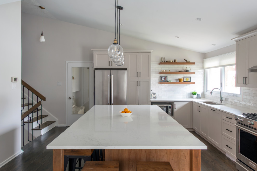 Example of a mid-sized transitional l-shaped medium tone wood floor, gray floor and vaulted ceiling open concept kitchen design in Ottawa with a double-bowl sink, shaker cabinets, gray cabinets, quartz countertops, white backsplash, subway tile backsplash, stainless steel appliances, an island and white countertops