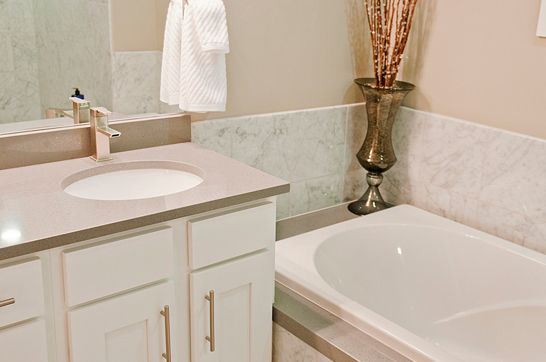 Inspiration for a mid-sized contemporary bathroom in Salt Lake City with an undermount sink, recessed-panel cabinets, white cabinets, quartzite benchtops, a drop-in tub, a shower/bathtub combo, a one-piece toilet, white tile and beige walls.