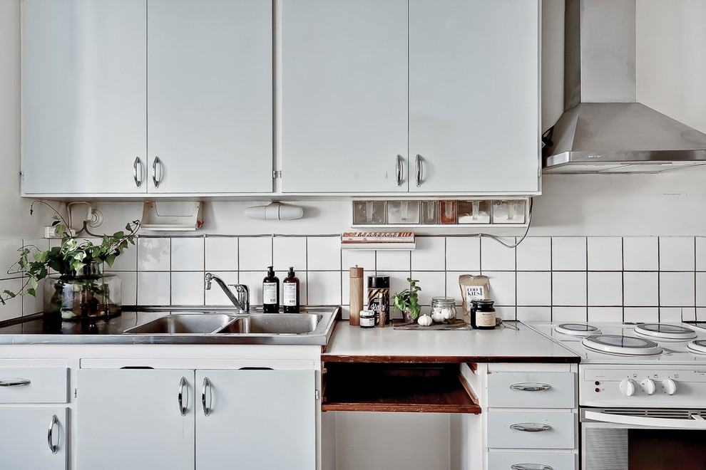 This is an example of a mid-sized scandinavian single-wall kitchen in Stockholm with a double-bowl sink, flat-panel cabinets, white cabinets, white splashback, ceramic splashback, white appliances and no island.