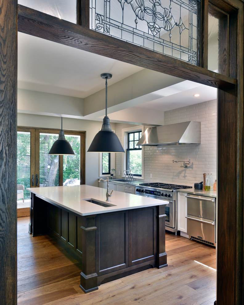 Inspiration for a mid-sized transitional galley medium tone wood floor eat-in kitchen remodel in Ottawa with an undermount sink, shaker cabinets, white cabinets, solid surface countertops, white backsplash, stainless steel appliances, an island and subway tile backsplash