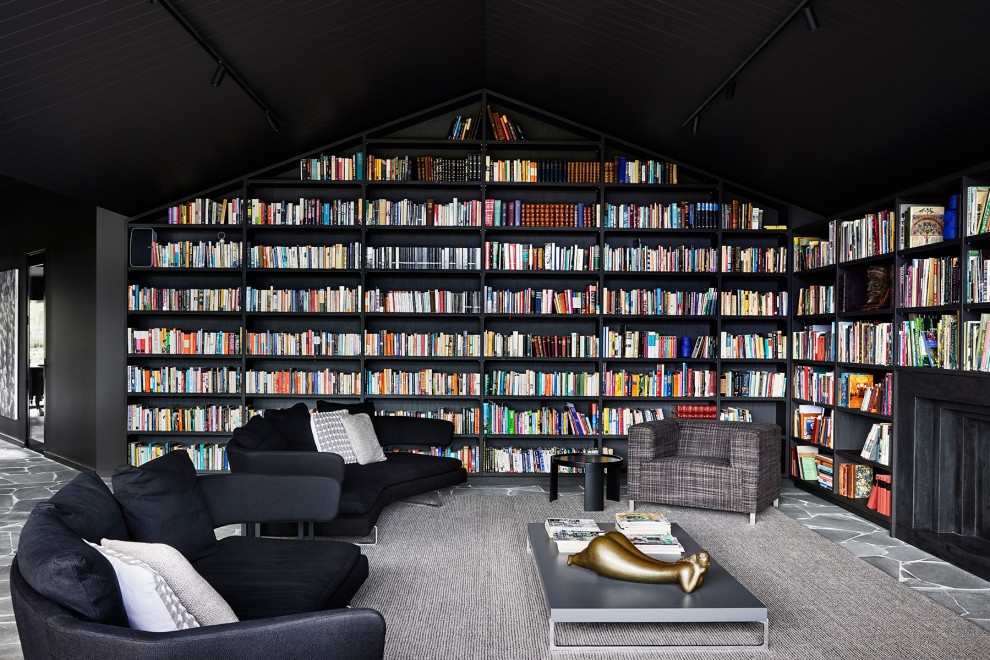 Cette photo montre une grande salle de séjour tendance avec une bibliothèque ou un coin lecture, un mur noir, une cheminée standard, un manteau de cheminée en métal, un plafond voûté et canapé noir.