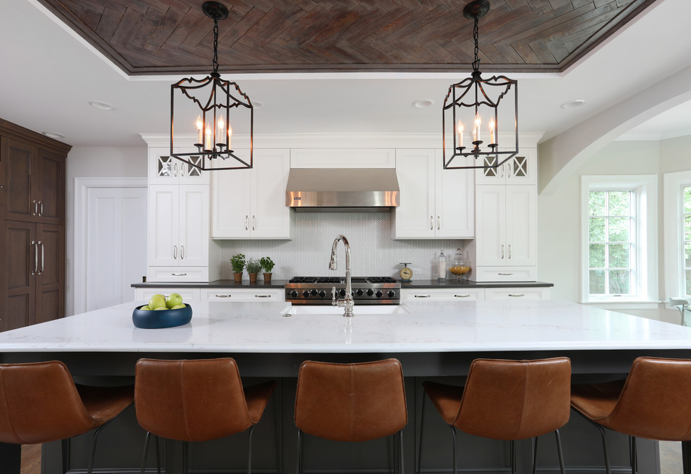 Photo of a large eclectic l-shaped open plan kitchen in Chicago with recessed-panel cabinets, with island, white cabinets, quartz benchtops, white splashback, ceramic splashback, stainless steel appliances, black benchtop, a farmhouse sink, medium hardwood floors and brown floor.