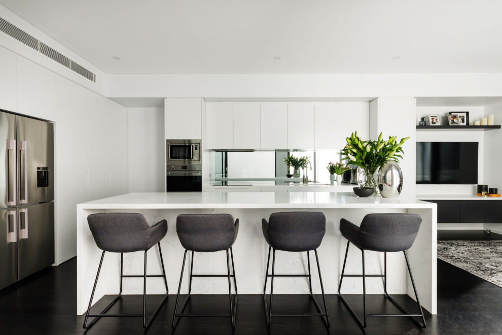 Inspiration for a small contemporary kitchen in London with flat-panel cabinets, white cabinets, quartzite benchtops, metallic splashback, glass sheet splashback, stainless steel appliances, dark hardwood floors, with island, black floor and white benchtop.