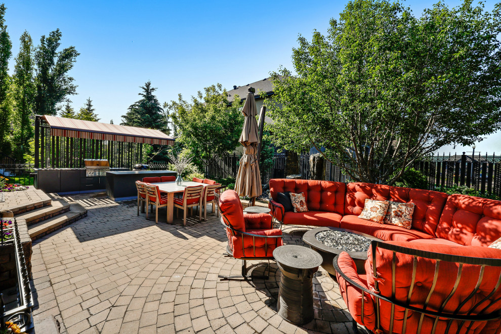 Photo of a large backyard patio in Calgary with a fire feature, brick pavers and an awning.