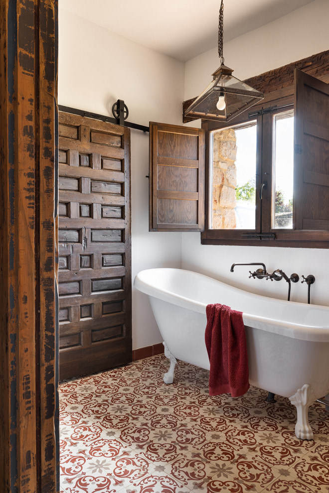 Ejemplo de cuarto de baño mediterráneo con bañera con patas, paredes blancas y suelo multicolor