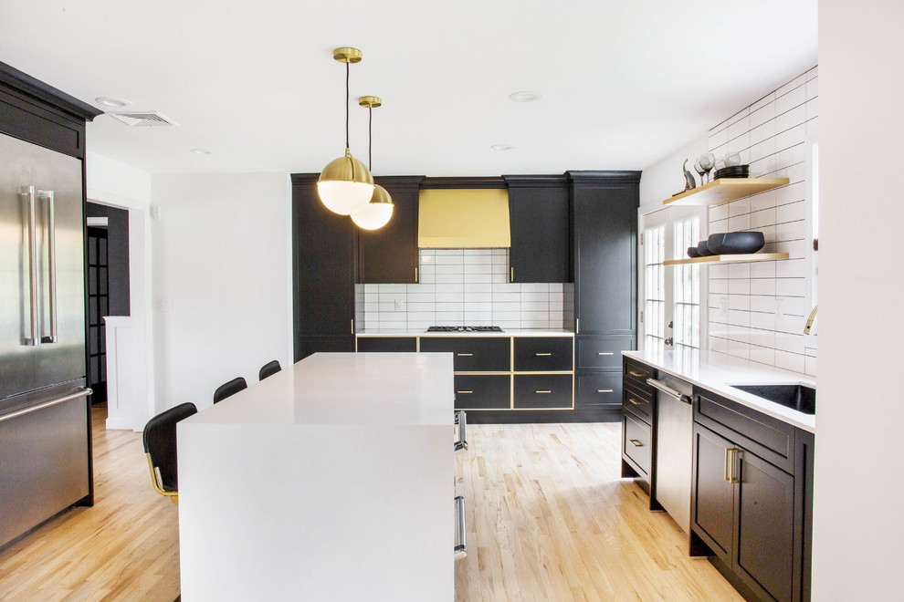 This is an example of a transitional u-shaped eat-in kitchen in New York with quartz benchtops, with island, white benchtop, an undermount sink, shaker cabinets, black cabinets, white splashback, ceramic splashback, stainless steel appliances, light hardwood floors and beige floor.