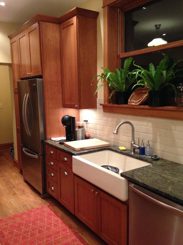Inspiration for a transitional galley eat-in kitchen remodel in Chicago with a farmhouse sink, shaker cabinets, medium tone wood cabinets, granite countertops, beige backsplash, subway tile backsplash and stainless steel appliances