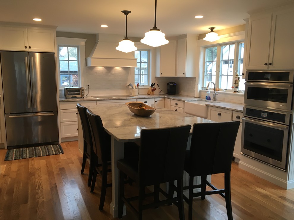 Transitional l-shaped medium tone wood floor eat-in kitchen photo in Boston with a farmhouse sink, shaker cabinets, white cabinets, white backsplash, porcelain backsplash, stainless steel appliances and an island