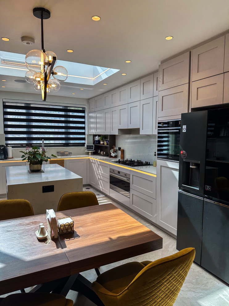 Large classic l-shaped kitchen/diner in London with a built-in sink, shaker cabinets, blue cabinets, quartz worktops, white splashback, engineered quartz splashback, integrated appliances, porcelain flooring, an island, beige floors, white worktops and feature lighting.