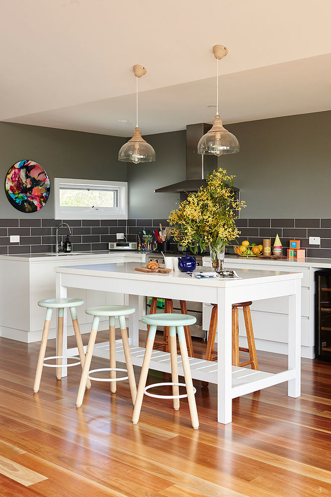 Large transitional l-shaped open plan kitchen in Melbourne with an undermount sink, white cabinets, quartz benchtops, ceramic splashback, stainless steel appliances, with island, orange floor, flat-panel cabinets, black splashback and medium hardwood floors.