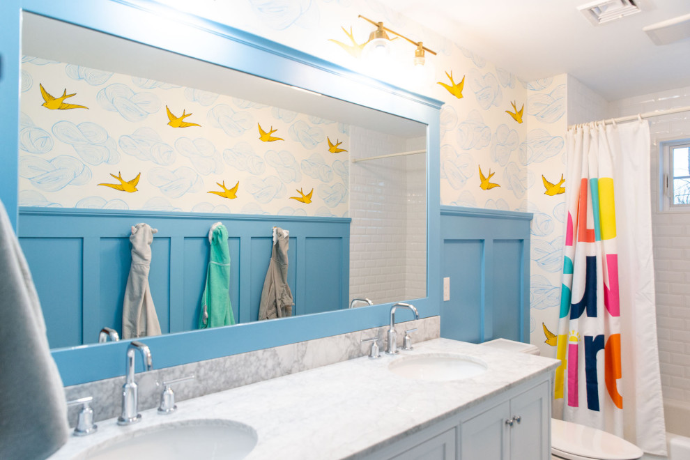 Mid-sized transitional kids bathroom in New York with shaker cabinets, white cabinets, a drop-in tub, a shower/bathtub combo, a one-piece toilet, blue walls, ceramic floors, a pedestal sink, engineered quartz benchtops, multi-coloured floor, a shower curtain, white benchtops, a double vanity, a built-in vanity and wallpaper.