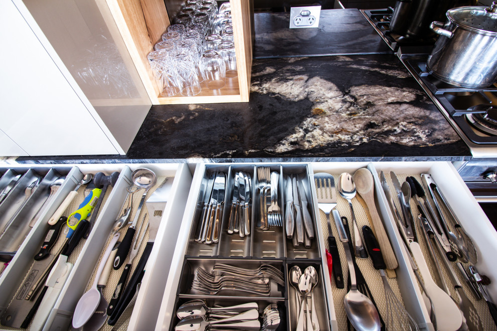 This is an example of a large modern u-shaped kitchen pantry in Central Coast with a double-bowl sink, flat-panel cabinets, beige cabinets, granite benchtops, metallic splashback, glass sheet splashback, stainless steel appliances, slate floors, a peninsula, brown floor and black benchtop.
