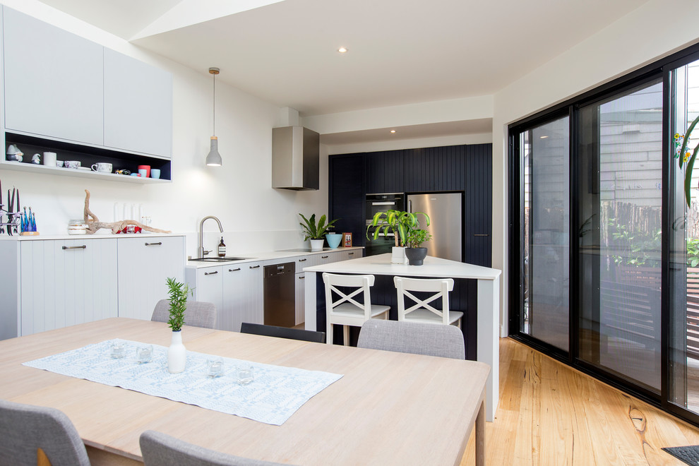 Photo of a small contemporary single-wall eat-in kitchen in Melbourne with an undermount sink, stainless steel appliances, medium hardwood floors, with island, brown floor and white benchtop.