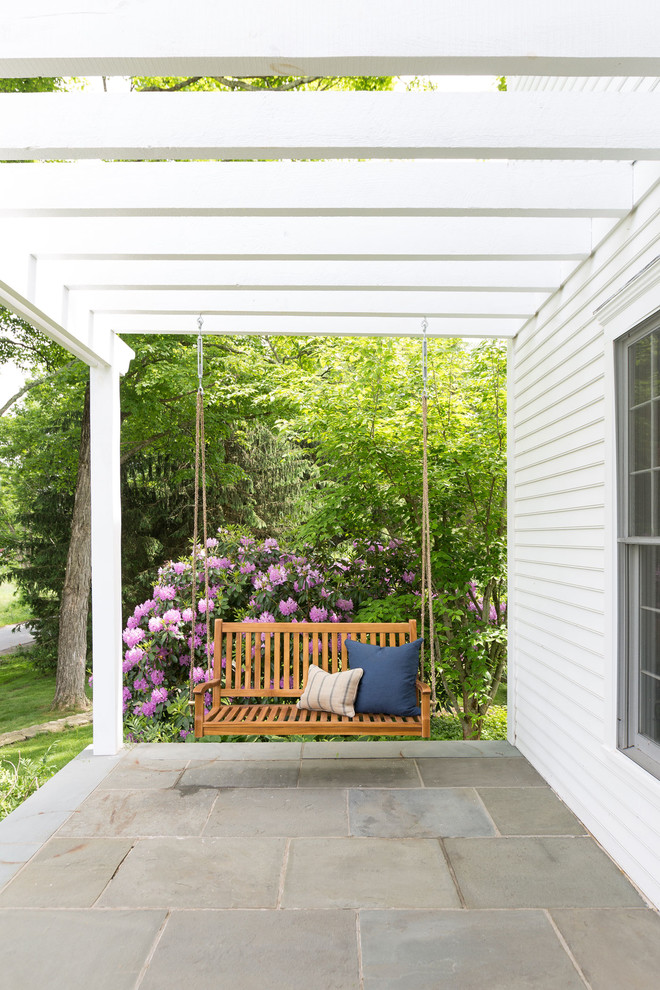 This is an example of a country front yard verandah in New York with concrete pavers and a pergola.