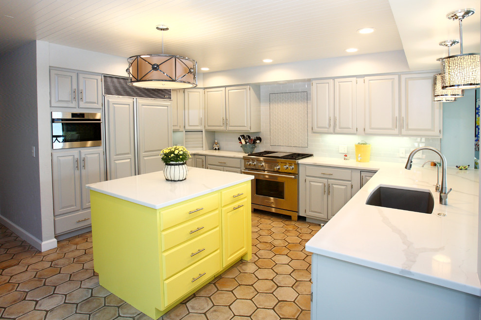 Photo of a transitional u-shaped open plan kitchen in Grand Rapids with an undermount sink, raised-panel cabinets, grey cabinets, white splashback, subway tile splashback, panelled appliances, terra-cotta floors, with island, beige floor and white benchtop.