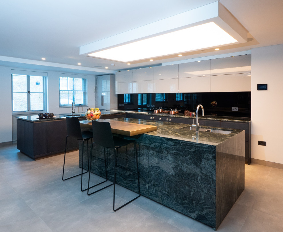 Design ideas for a modern open plan kitchen in London with a drop-in sink, flat-panel cabinets, dark wood cabinets, granite benchtops, black appliances, porcelain floors, with island, grey floor, green benchtop and coffered.