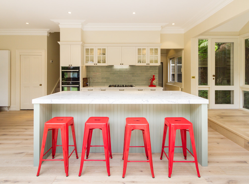 Photo of a mid-sized traditional galley eat-in kitchen in Melbourne with an undermount sink, shaker cabinets, white cabinets, quartz benchtops, green splashback, subway tile splashback, black appliances, light hardwood floors, with island, beige floor and white benchtop.