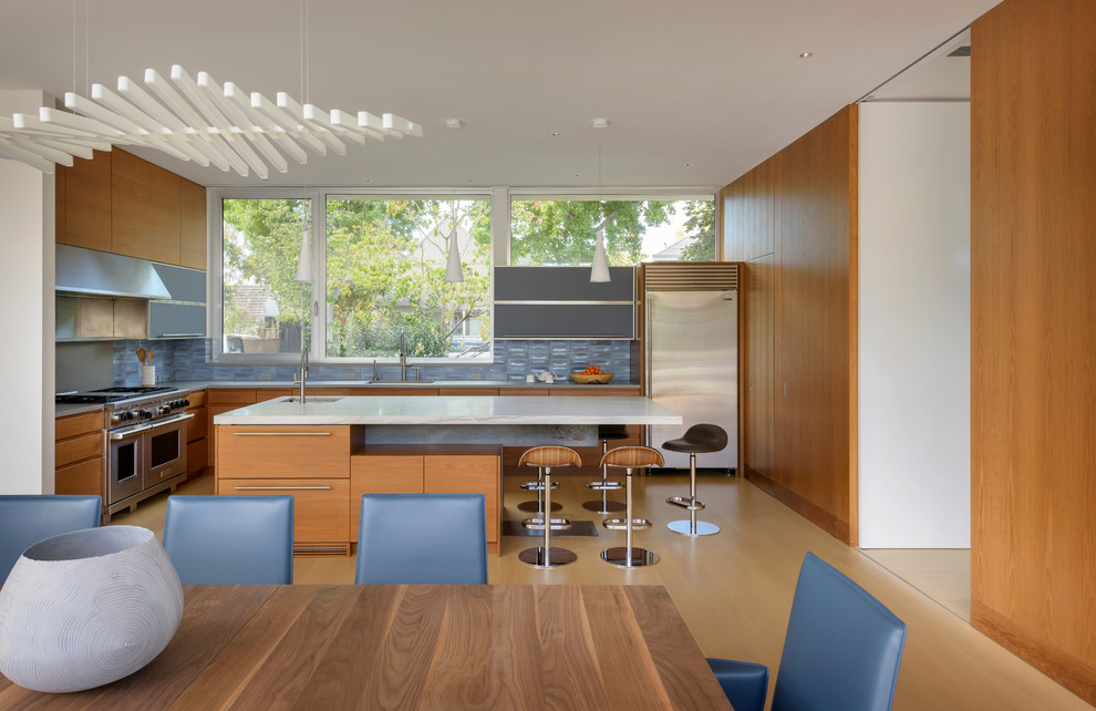 Modern l-shaped eat-in kitchen in San Francisco with an undermount sink, louvered cabinets, medium wood cabinets, marble benchtops, blue splashback, ceramic splashback, stainless steel appliances, medium hardwood floors, with island, brown floor and white benchtop.
