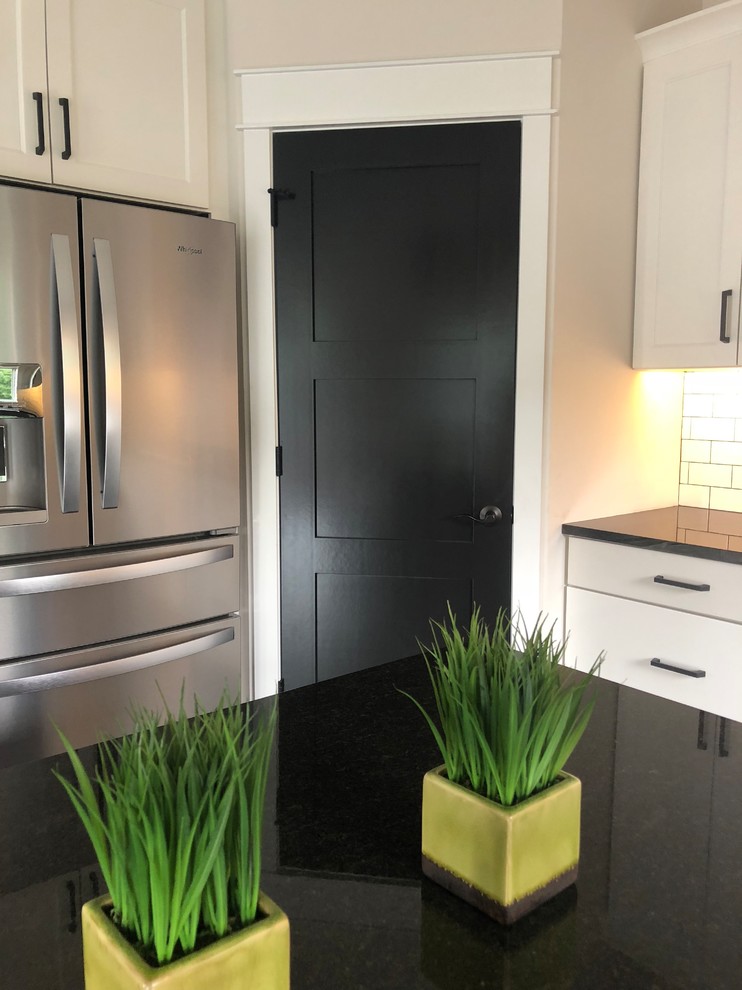 Example of a mid-sized transitional u-shaped dark wood floor and brown floor kitchen pantry design in Minneapolis with a farmhouse sink, recessed-panel cabinets, white cabinets, granite countertops, white backsplash, subway tile backsplash, stainless steel appliances, an island and black countertops