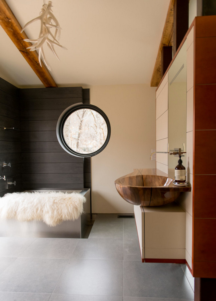 This is an example of a large modern master bathroom in Other with a vessel sink, furniture-like cabinets, light wood cabinets, wood benchtops, a japanese tub, a shower/bathtub combo, a wall-mount toilet, gray tile, ceramic tile and ceramic floors.