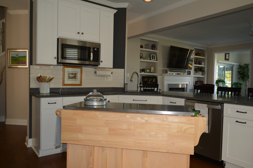 Foto på ett mellanstort vintage grå kök, med en undermonterad diskho, släta luckor, vita skåp, bänkskiva i kvarts, vitt stänkskydd, stänkskydd i tunnelbanekakel, rostfria vitvaror, en köksö och brunt golv