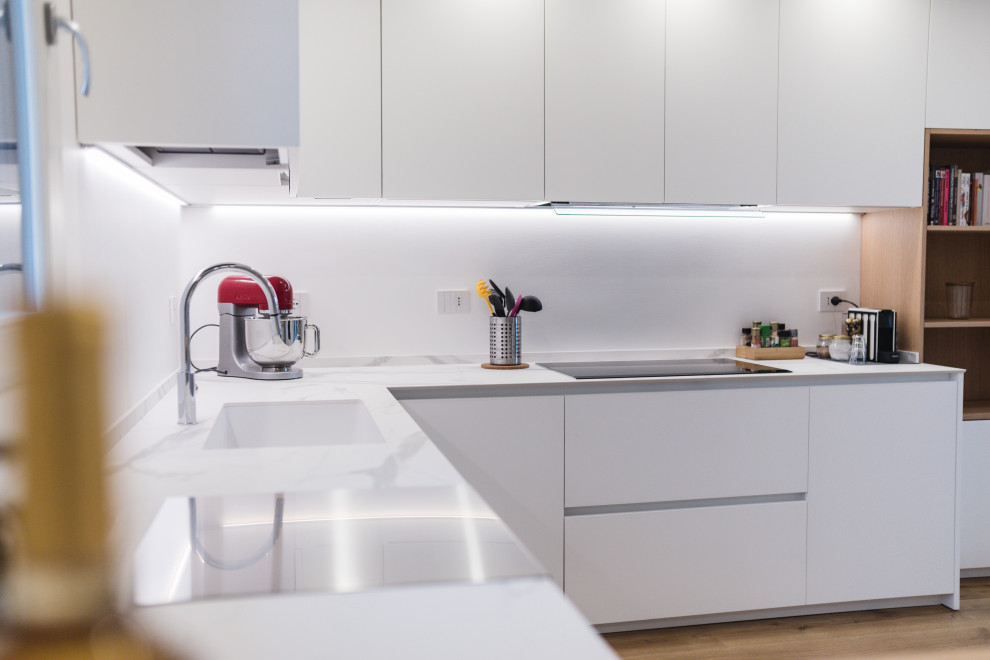 Design ideas for a mid-sized contemporary u-shaped open plan kitchen in Milan with a drop-in sink, flat-panel cabinets, white cabinets, quartz benchtops, black appliances, laminate floors, with island and white benchtop.