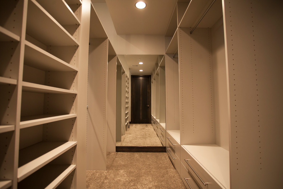 This is an example of a mid-sized modern gender-neutral walk-in wardrobe in Omaha with flat-panel cabinets, white cabinets, carpet and beige floor.