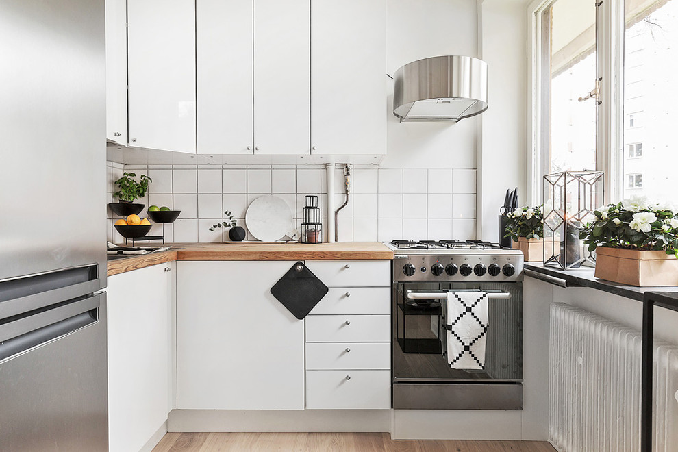 Inspiration for a small scandinavian l-shaped kitchen in Stockholm with flat-panel cabinets, white cabinets, wood benchtops, white splashback, stainless steel appliances, no island and medium hardwood floors.