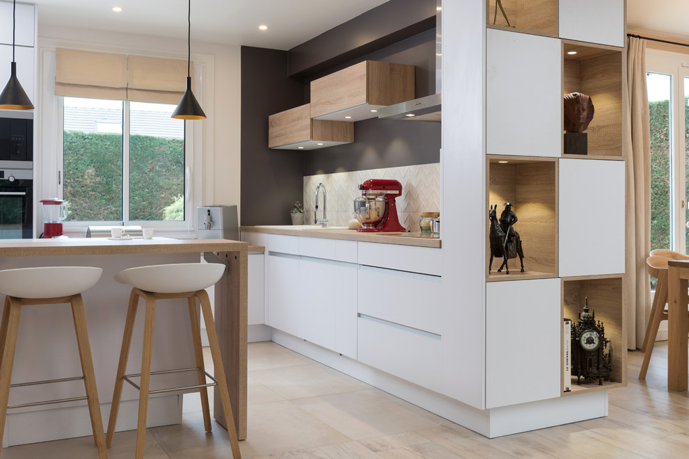 This is an example of a mid-sized contemporary single-wall open plan kitchen in Paris with beaded inset cabinets, white cabinets, marble benchtops, white splashback, stainless steel appliances, light hardwood floors, with island and beige floor.