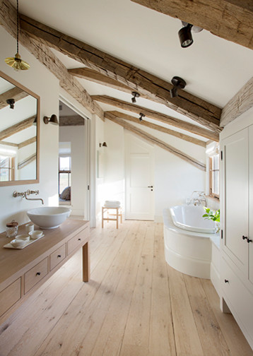 This is an example of a mid-sized country master bathroom in Boston with flat-panel cabinets, grey cabinets, a drop-in tub, white walls, light hardwood floors, a vessel sink, wood benchtops and beige floor.