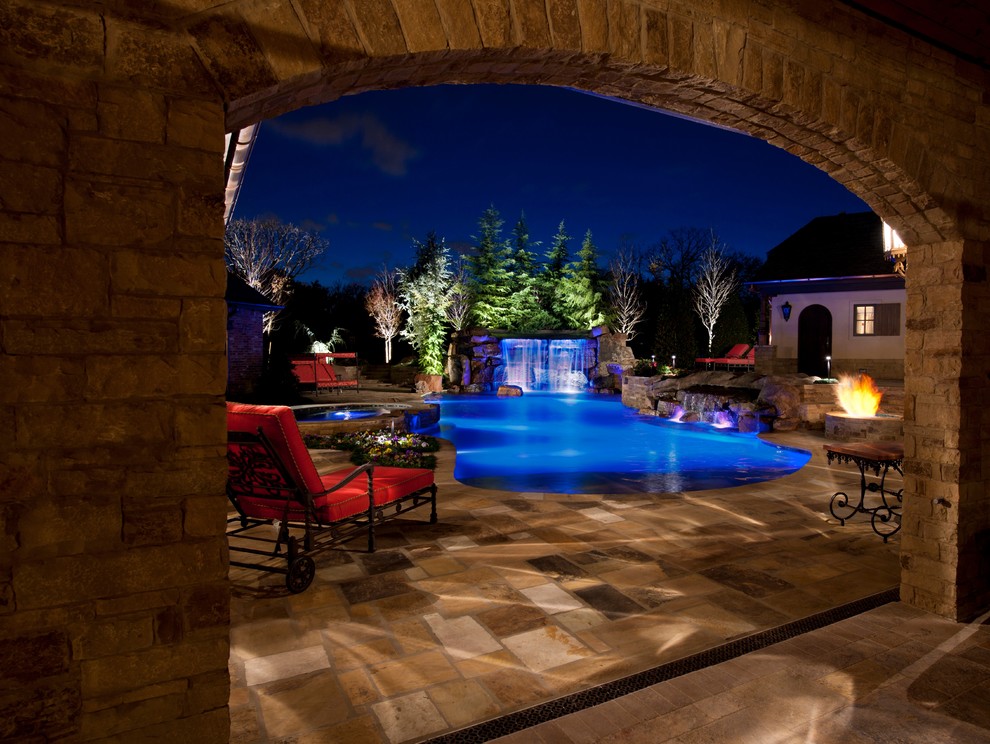 Design ideas for a large mediterranean backyard custom-shaped natural pool in Oklahoma City with natural stone pavers and a hot tub.