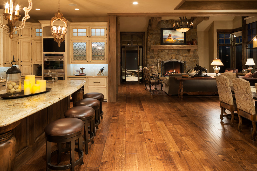 This is an example of an expansive country u-shaped kitchen in Minneapolis with a farmhouse sink, raised-panel cabinets, distressed cabinets, granite benchtops, beige splashback, stone tile splashback, stainless steel appliances, with island, dark hardwood floors and brown floor.