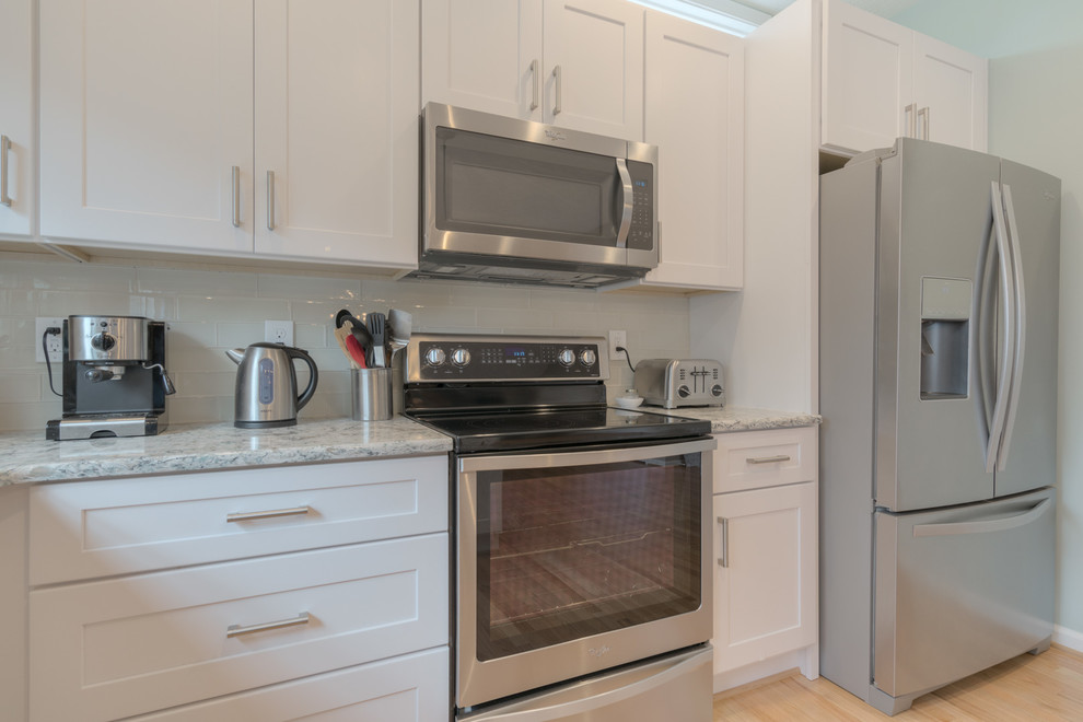 Example of a mid-sized transitional u-shaped light wood floor eat-in kitchen design with an undermount sink, shaker cabinets, white cabinets, quartz countertops, beige backsplash, glass tile backsplash, stainless steel appliances and a peninsula