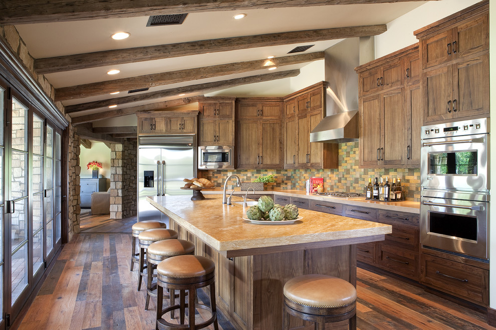 Photo of a large country l-shaped separate kitchen in Phoenix with stainless steel appliances, a farmhouse sink, shaker cabinets, dark wood cabinets, marble benchtops, multi-coloured splashback, stone tile splashback, dark hardwood floors, with island and brown floor.