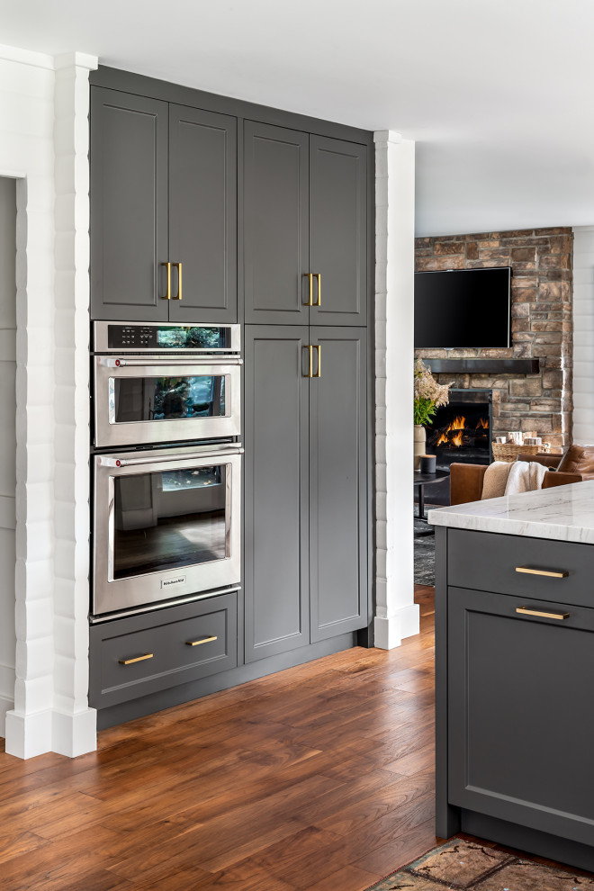 Mid-sized mountain style medium tone wood floor kitchen photo in Toronto with a double-bowl sink, recessed-panel cabinets, gray cabinets, quartzite countertops, white backsplash, mosaic tile backsplash, stainless steel appliances, an island and white countertops
