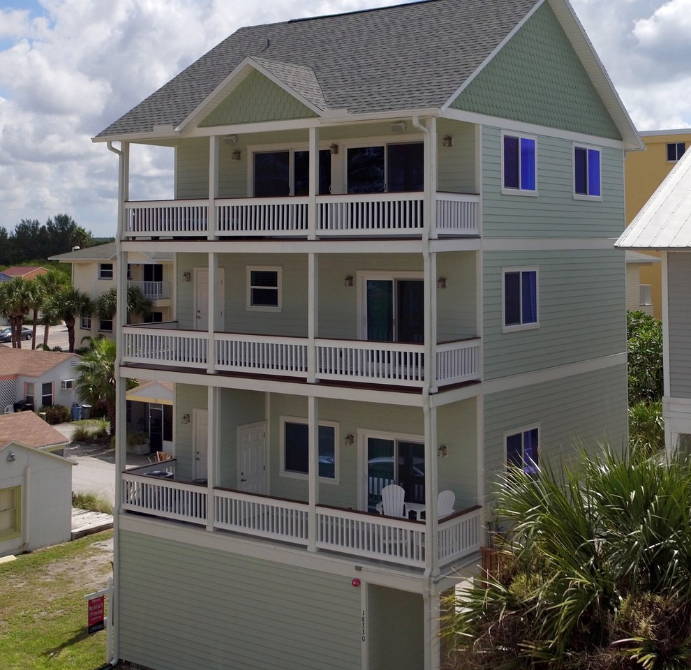 This is an example of a large beach style green exterior in Tampa with wood siding, a gable roof and four or more storeys.
