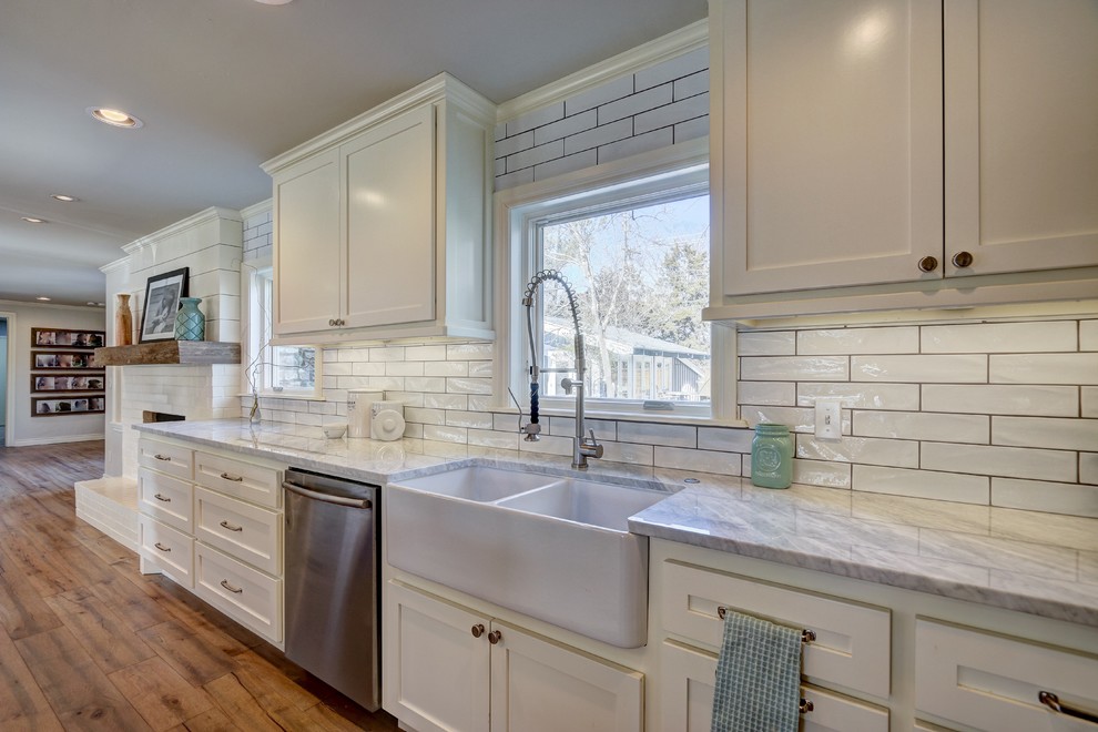 Large industrial open plan kitchen in Oklahoma City with a farmhouse sink, shaker cabinets, white cabinets, white splashback, subway tile splashback, stainless steel appliances, medium hardwood floors and multiple islands.
