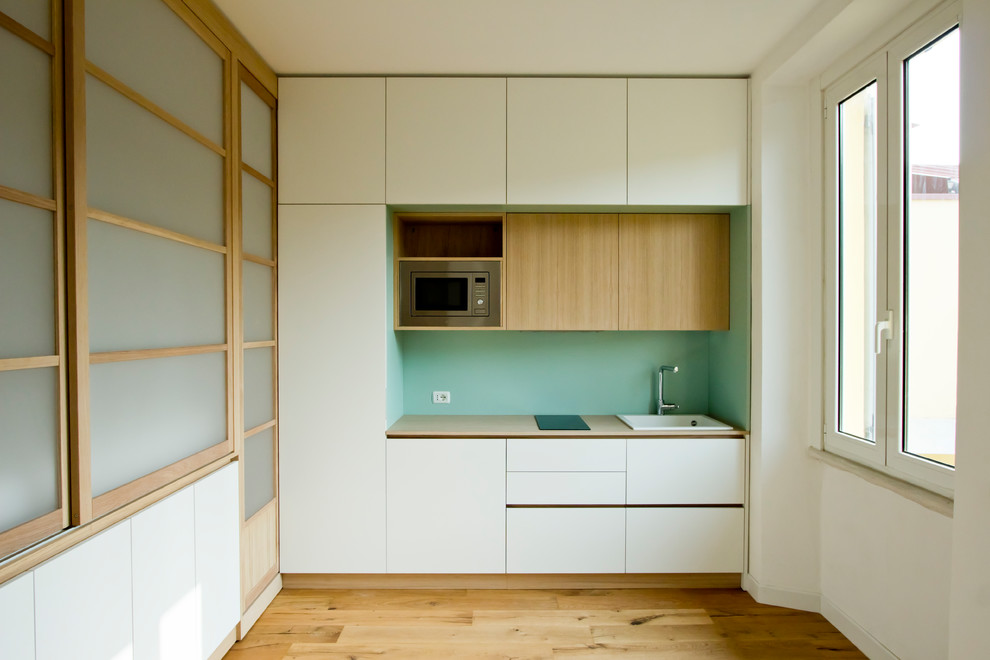 Design ideas for a small scandinavian single-wall open plan kitchen in Milan with a drop-in sink, flat-panel cabinets, white cabinets, wood benchtops, green splashback, timber splashback, stainless steel appliances, light hardwood floors, brown floor and brown benchtop.