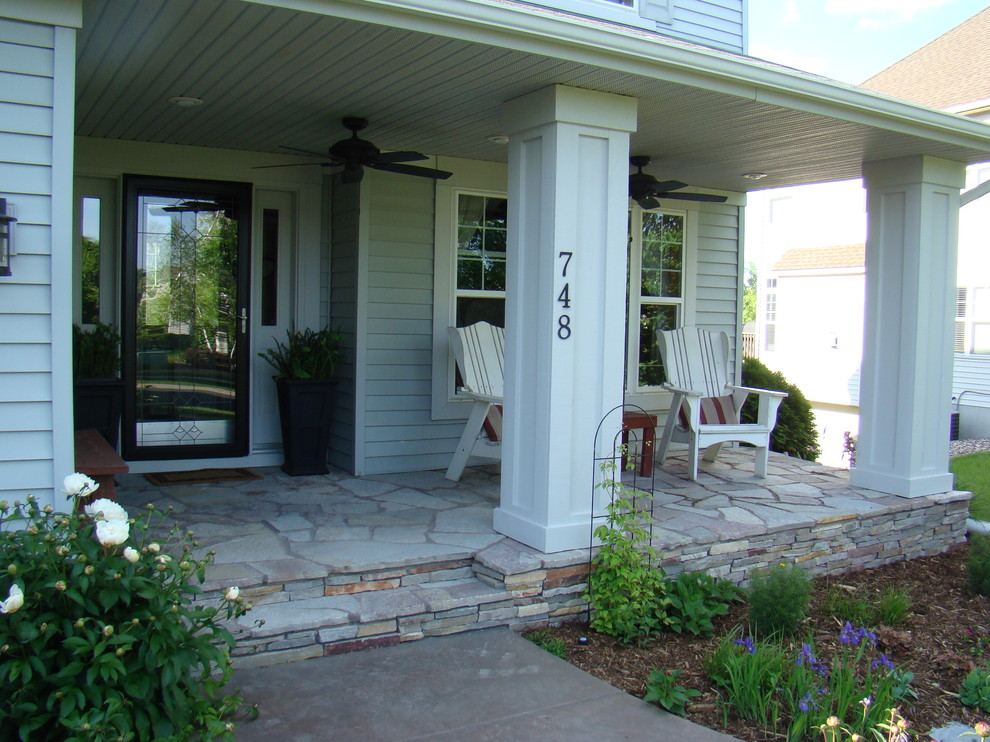 This is an example of a front yard verandah in Minneapolis with natural stone pavers and a roof extension.