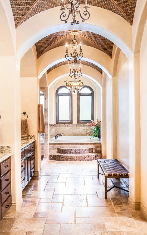 Photo of a mediterranean bathroom in Houston with raised-panel cabinets, dark wood cabinets, a drop-in tub, beige tile and beige walls.