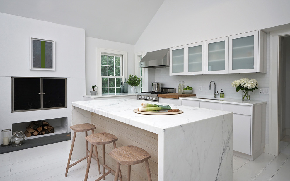 This is an example of a modern kitchen pantry in Boston with an undermount sink, flat-panel cabinets, white cabinets, glass benchtops, white splashback, marble splashback, stainless steel appliances, painted wood floors, with island, white floor and white benchtop.