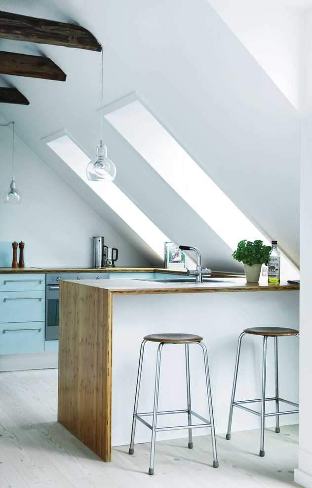 Small scandinavian u-shaped open plan kitchen in Copenhagen with a drop-in sink, flat-panel cabinets, turquoise cabinets, wood benchtops, stainless steel appliances, light hardwood floors and a peninsula.